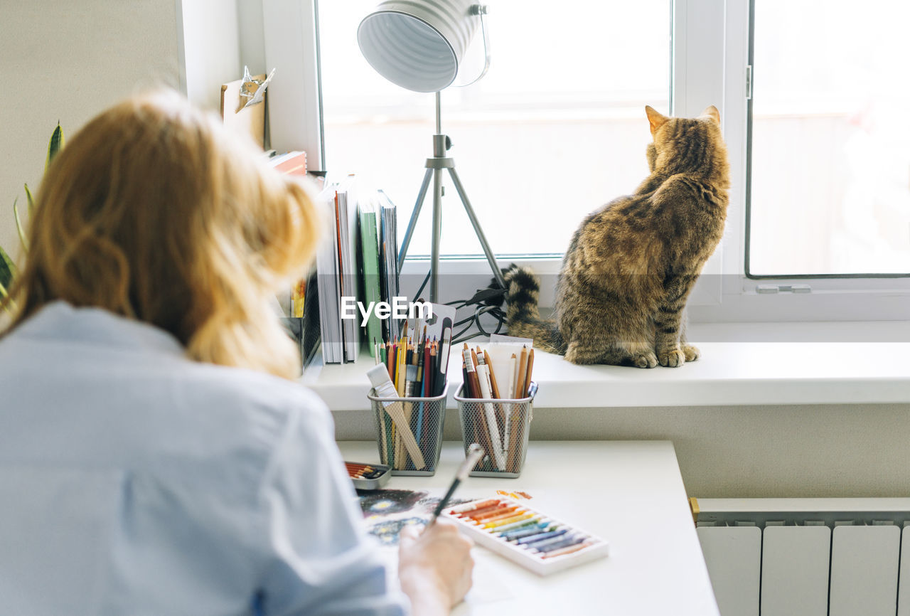 Rear view of woman with cat sitting on table