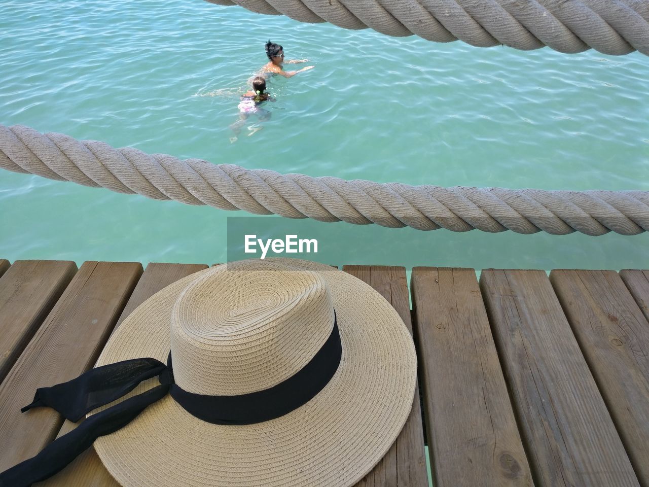 High angle view of hat on pier above woman with daughter swimming in sea