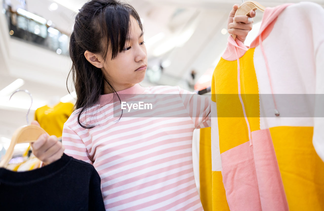 Beautiful asian child girl choosing clothes in clothing shop in shopping center,mall