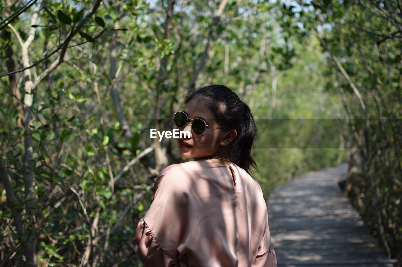 Young woman wearing sunglasses standing by plants on street