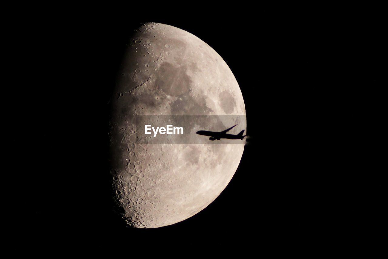 Low angle view of airplane flying by moon at night