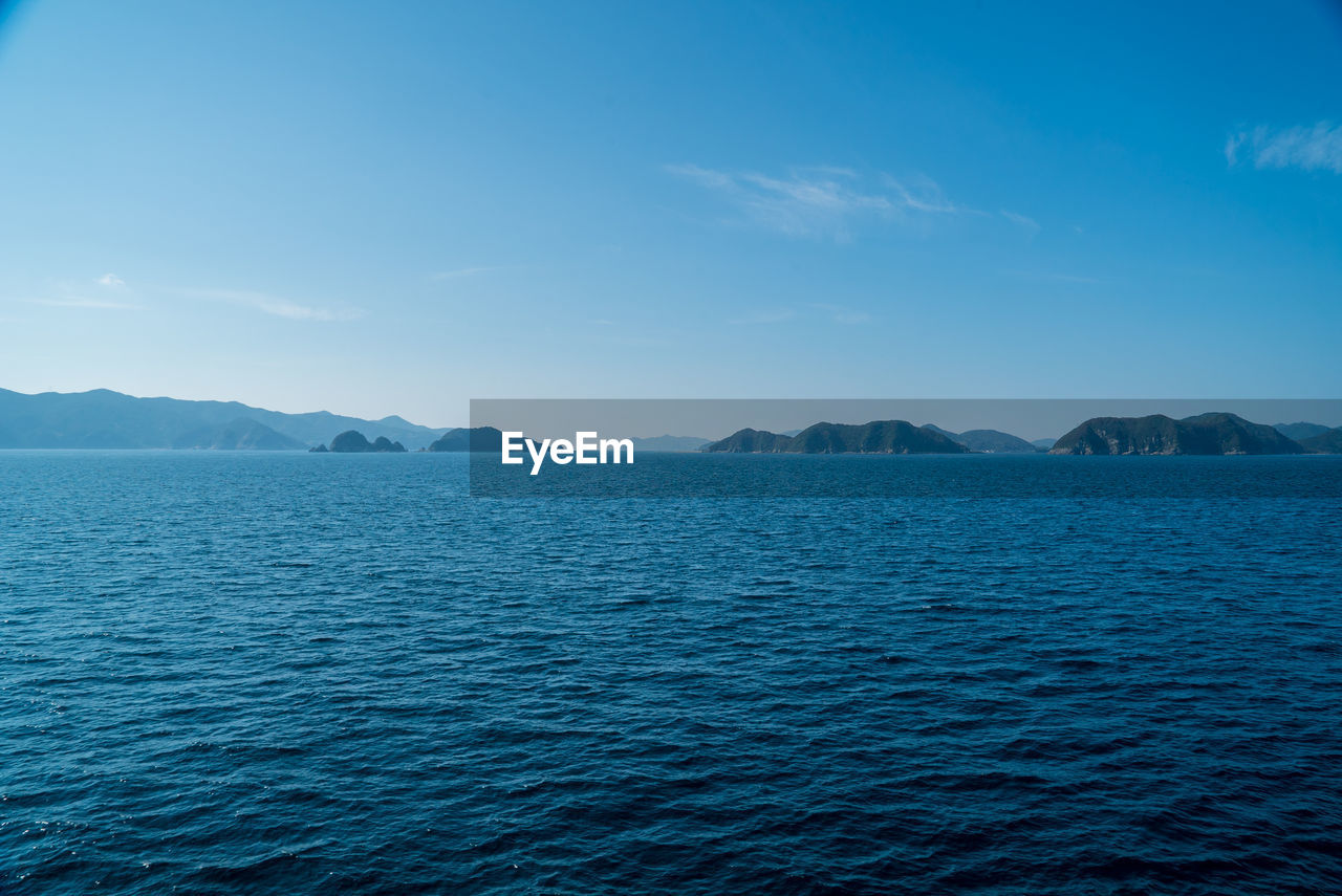 SCENIC VIEW OF SEA BY MOUNTAINS AGAINST BLUE SKY