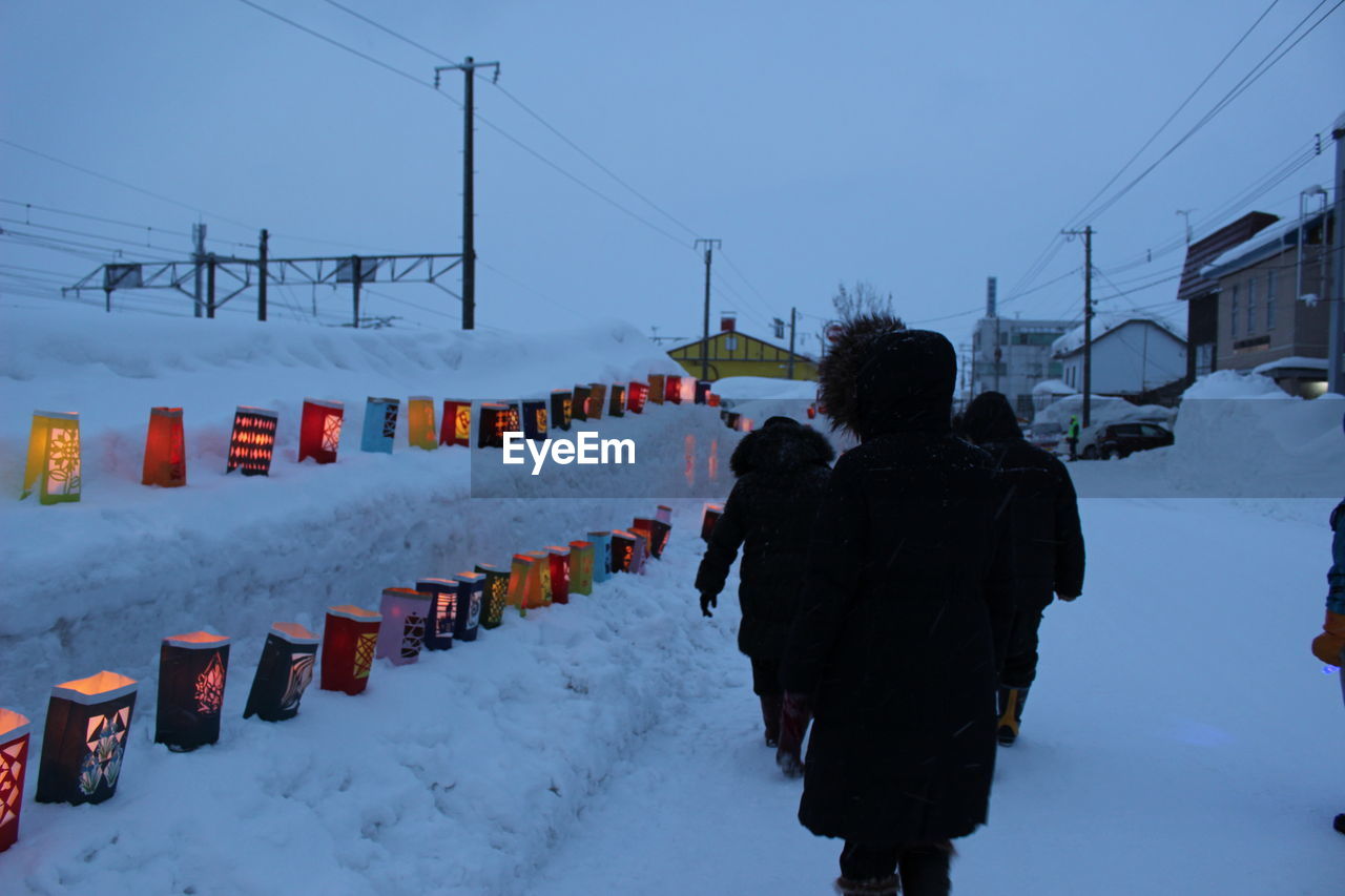 Rear view of people walking on snow covered field against sky