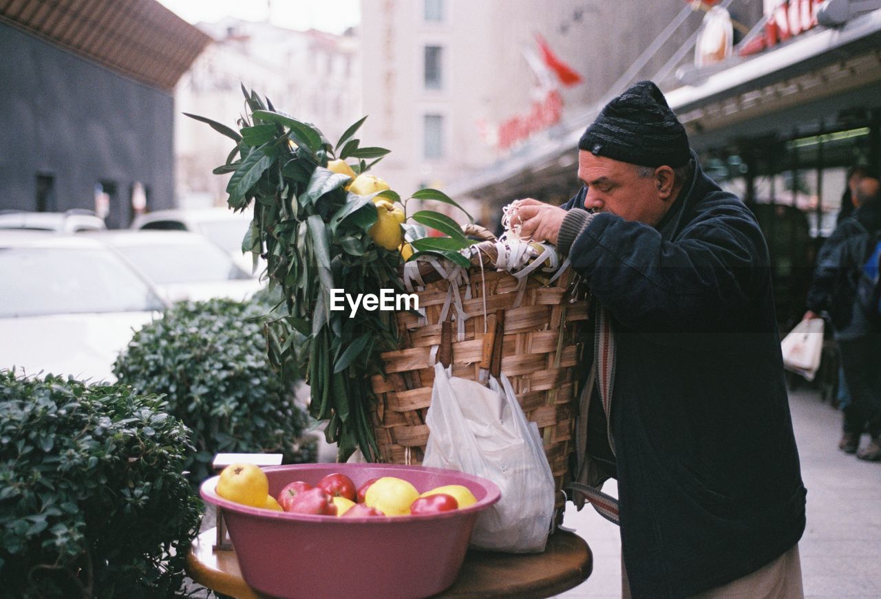 Side view of man with wicker basket standing in city