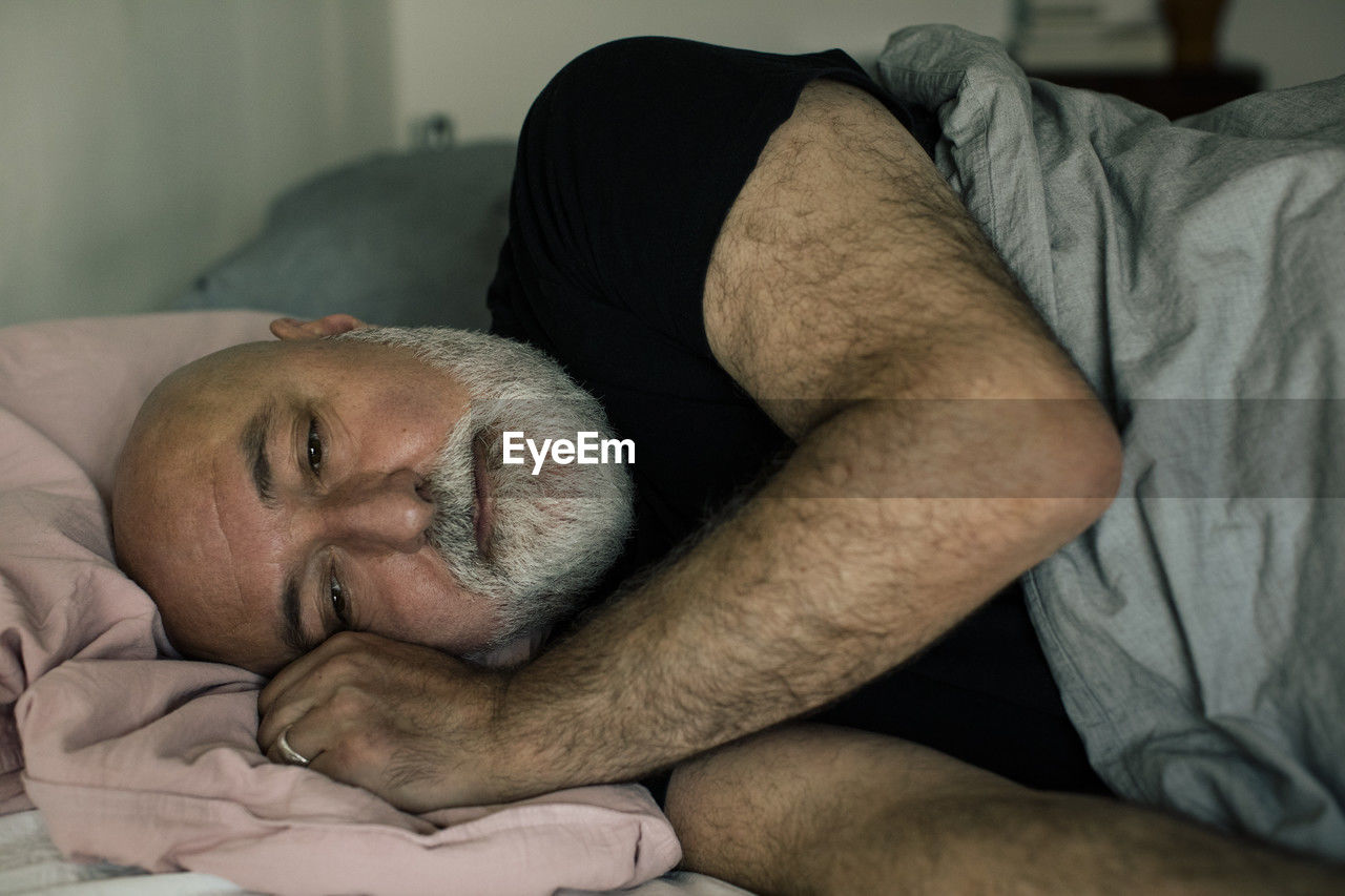 Stressed mature man lying down on bed at home
