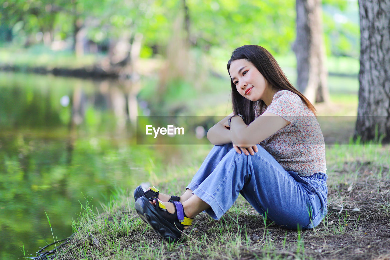 Beautiful asian woman sitting alone on the waterside in public park