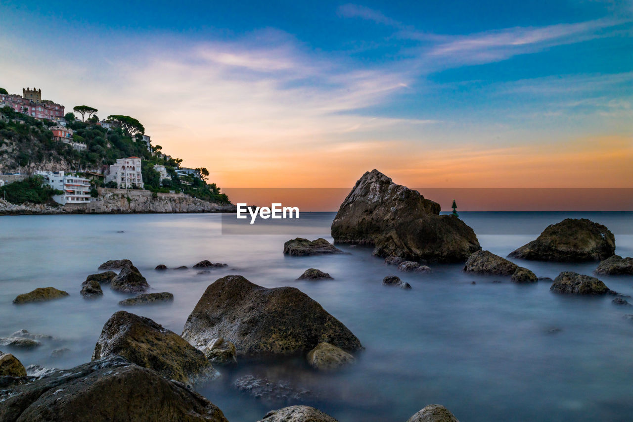 Rocks on beach against sky during sunset