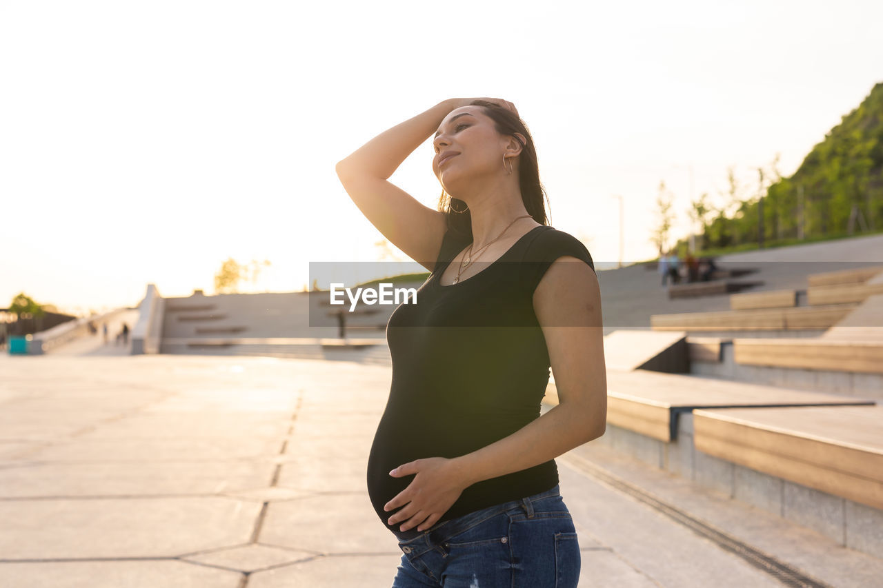 FULL LENGTH OF YOUNG WOMAN STANDING IN FRONT OF BUILT STRUCTURE