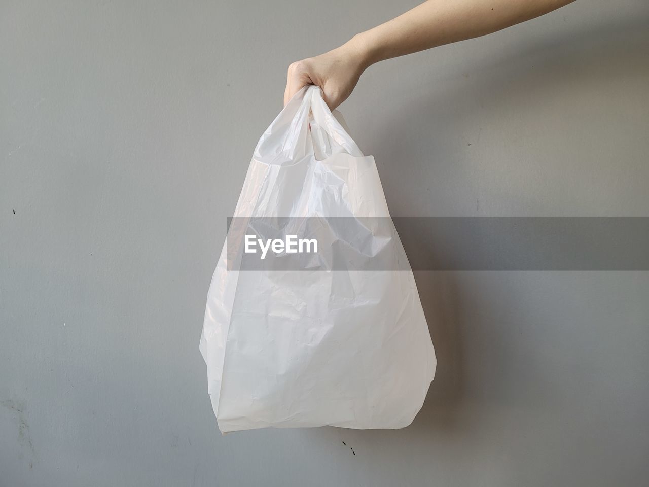 white, handbag, bag, plastic bag, indoors, one person, hand, shopping bag, studio shot, holding, plastic, adult, women, tote bag, fashion accessory, dress, close-up, clothing, gray, copy space
