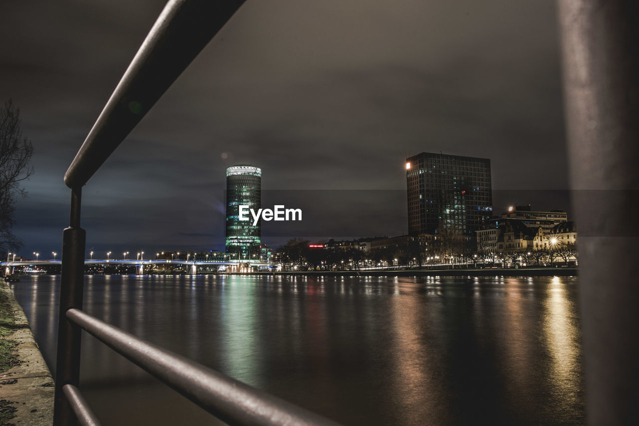 Illuminated buildings by river against sky at night