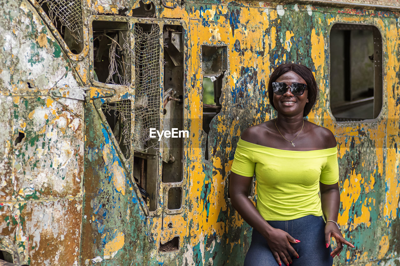 Happy africa woman from ghana stands in front of an old broken helicopter