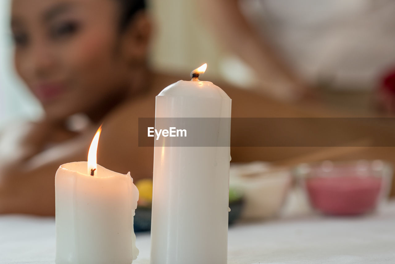 Close-up of candles with woman relaxing in background at spa