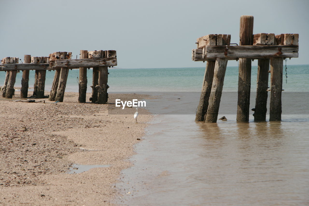 WOODEN POSTS ON BEACH AGAINST SKY