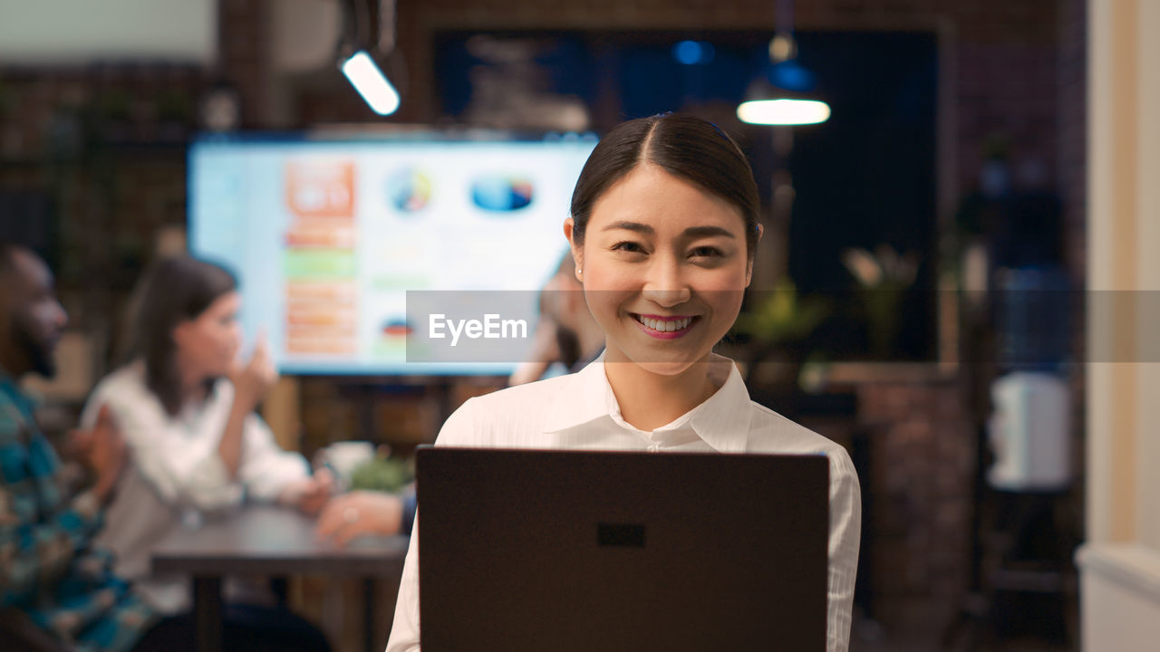 portrait of smiling young woman using digital tablet while standing in library