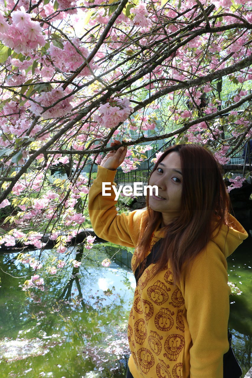 PORTRAIT OF WOMAN STANDING BY PINK FLOWER