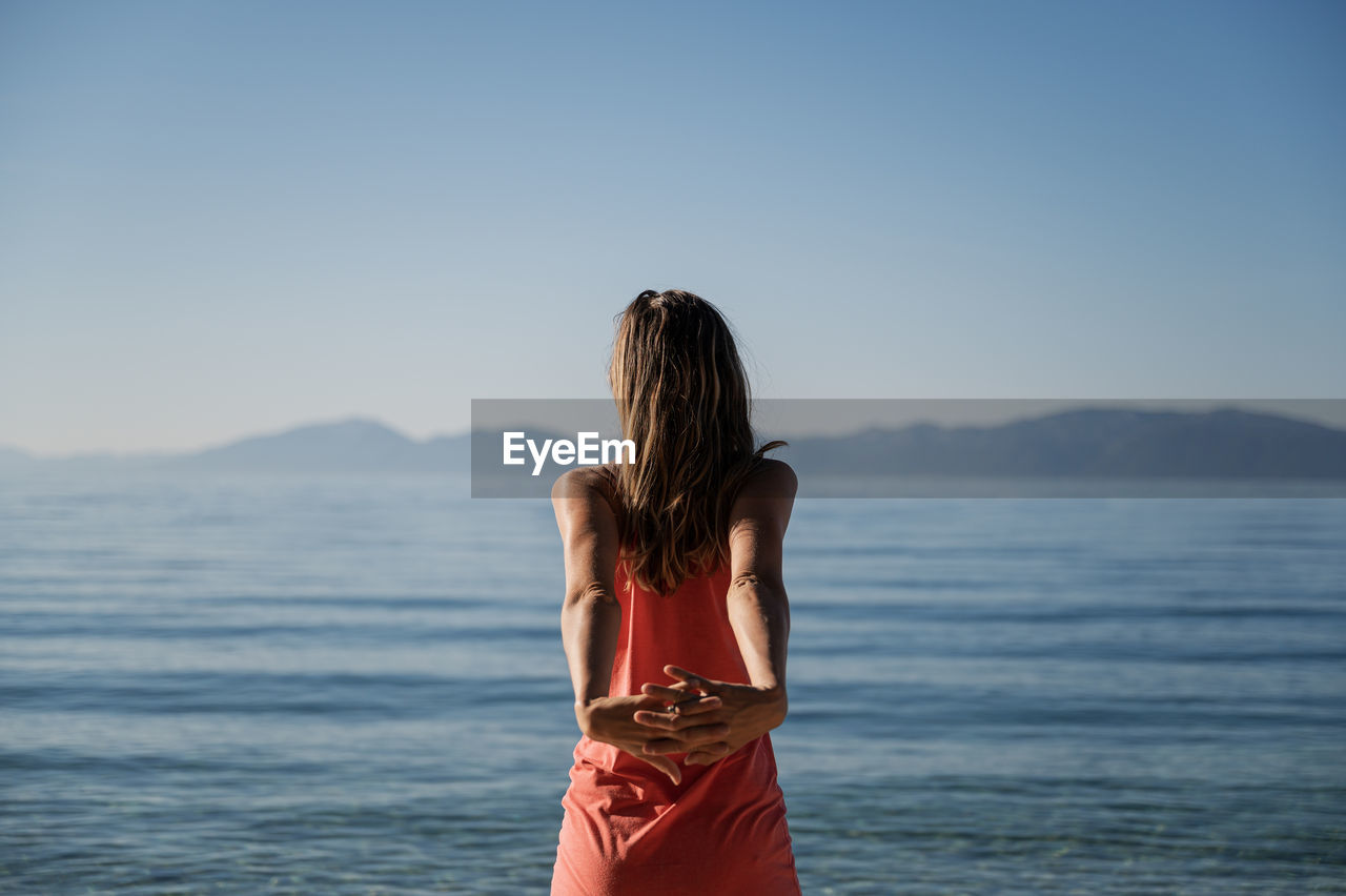 Rear view of woman standing by sea against sky