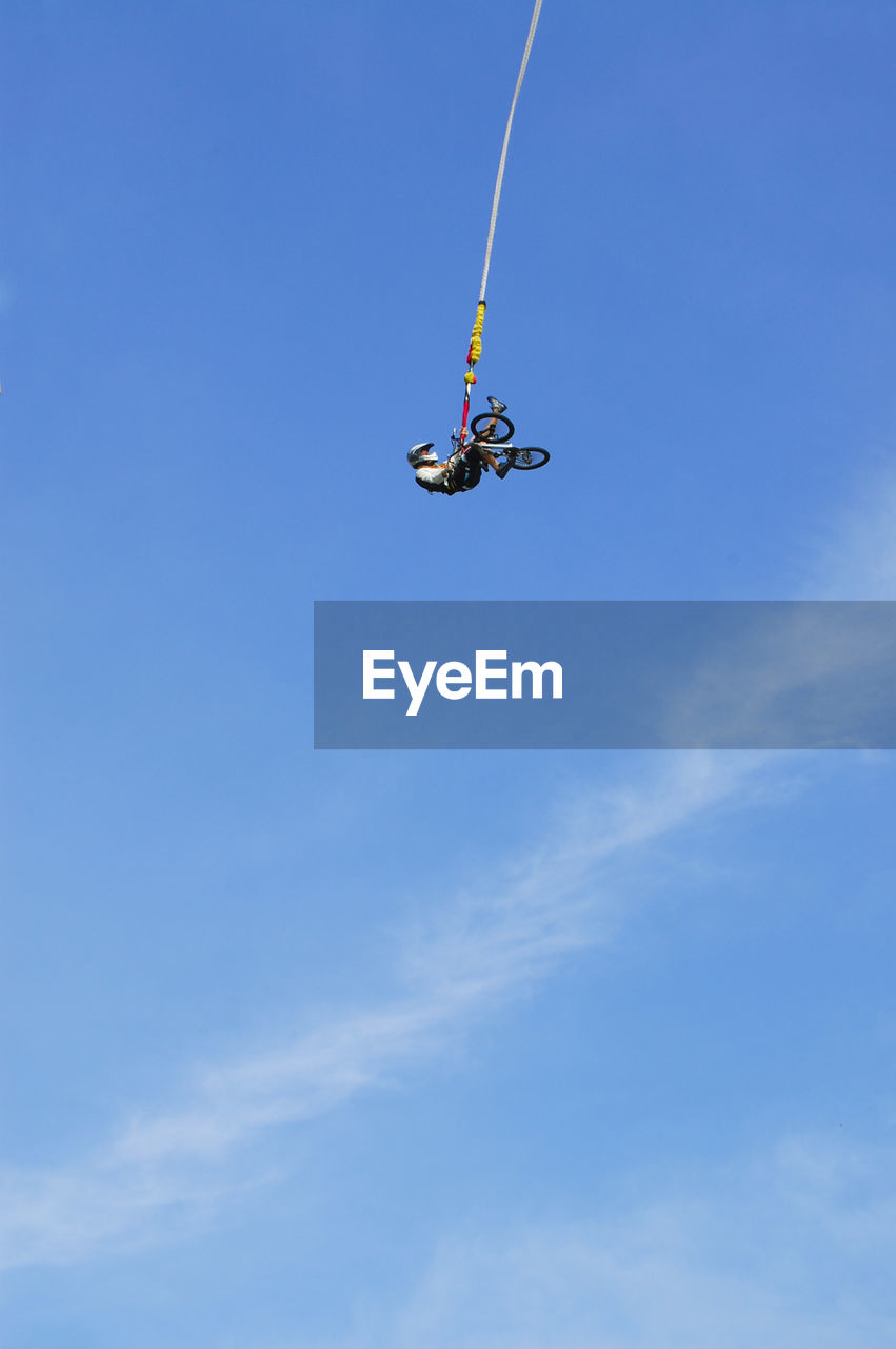 Low angle view of man with bicycle hanging against blue sky