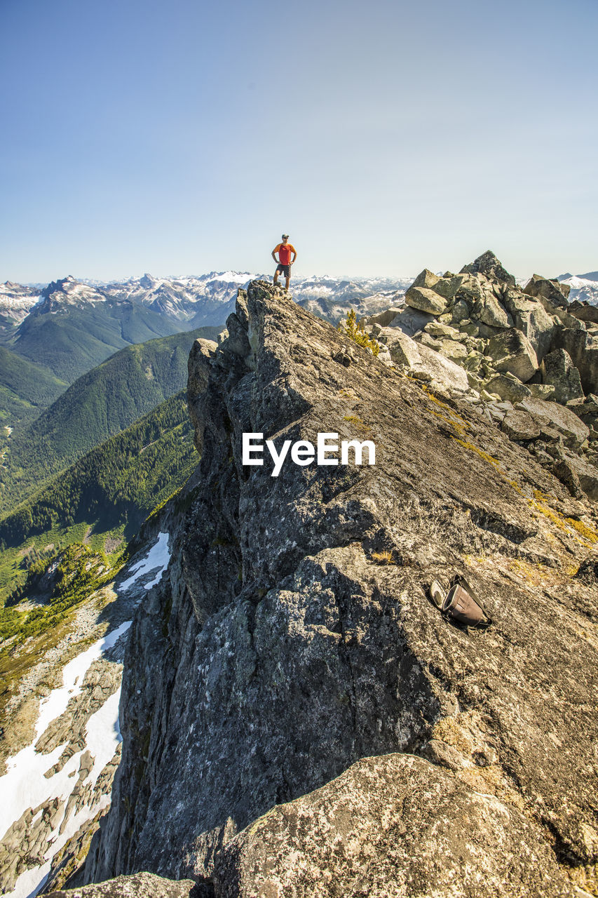 Trail runner stands on mountain summit, edge of a cliff.