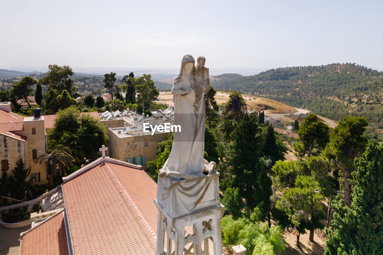 STATUE BY TREES AND BUILDING AGAINST SKY