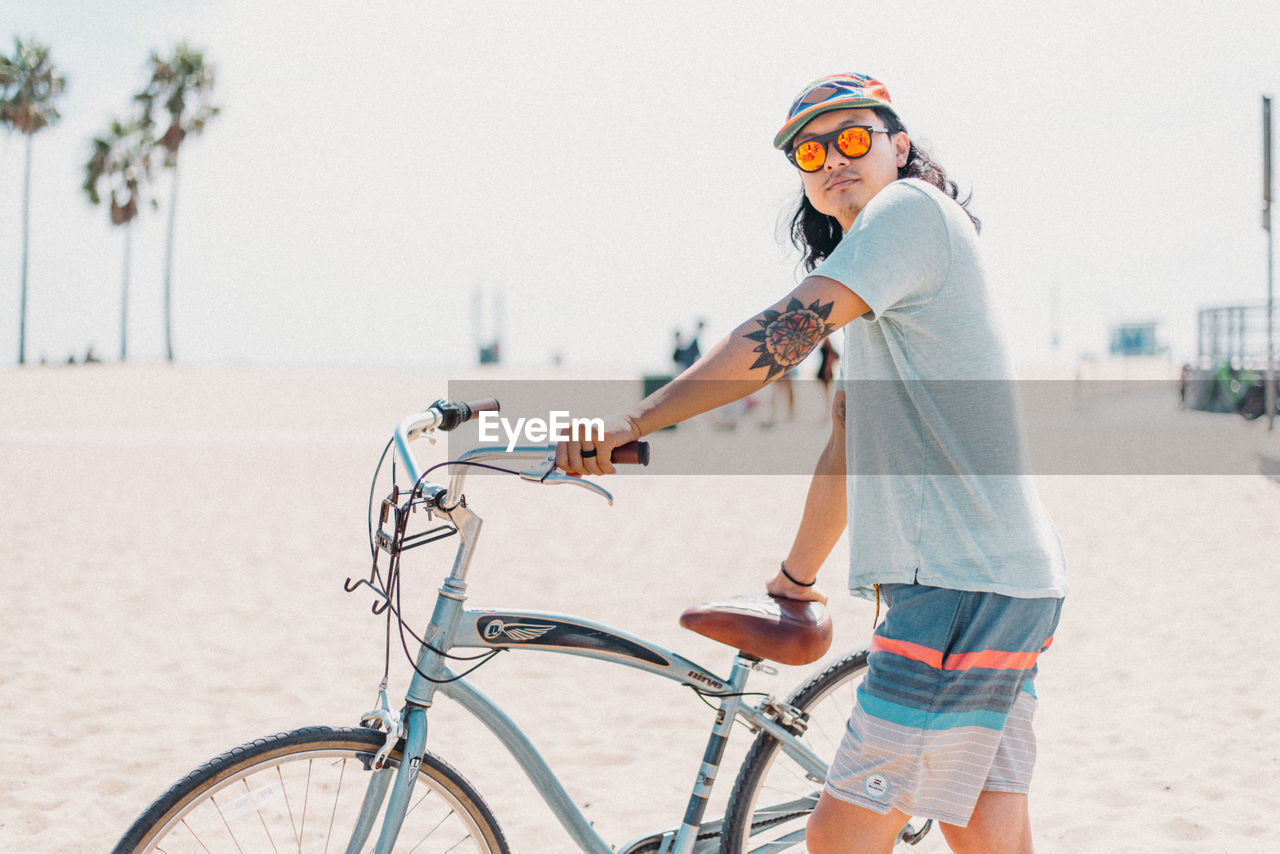 YOUNG WOMAN RIDING BICYCLE ON BEACH AGAINST CLEAR SKY