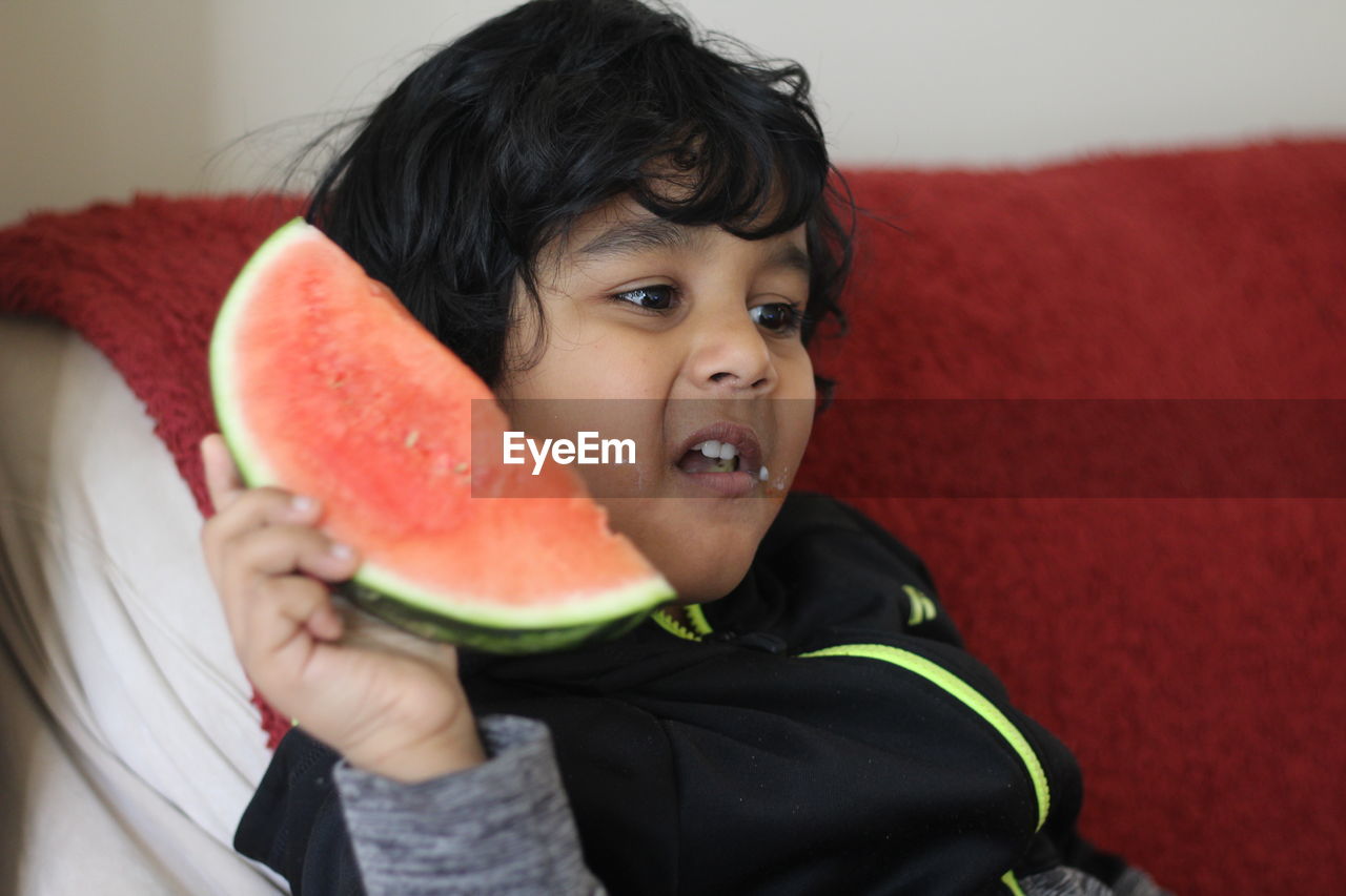 Close-up of cute boy holding watermelon at home