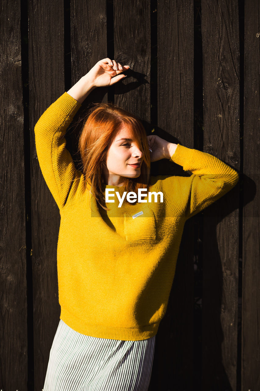 Beautiful young woman in yellow sweater standing against fence