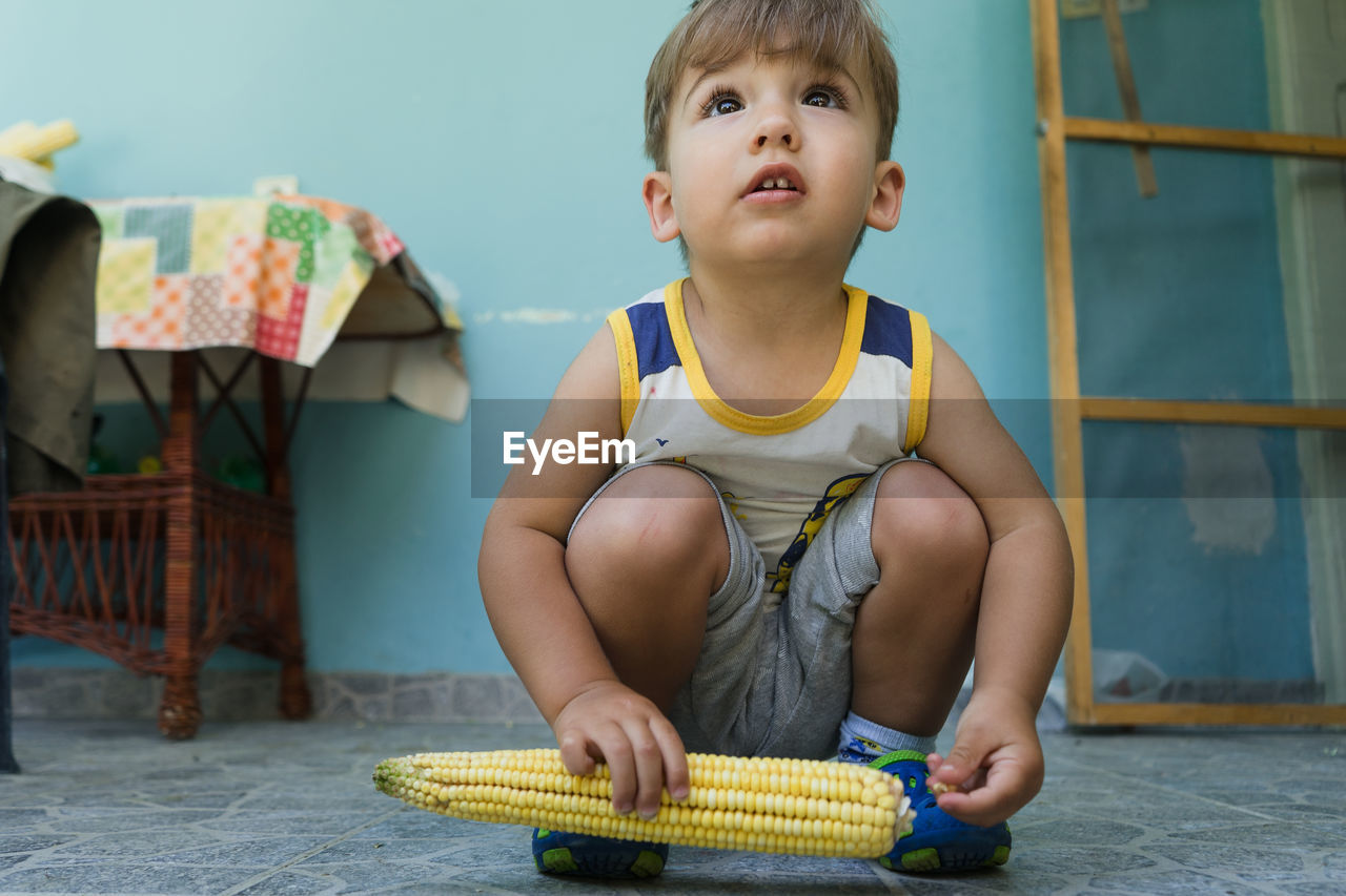 Full length of cute boy with corn crouching at home