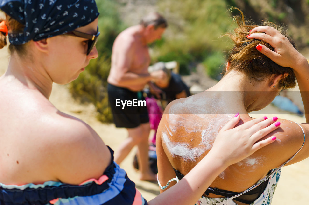 Woman applying lotion to friend at beach