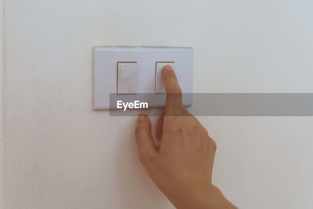 Cropped hand of person over light switch on wall