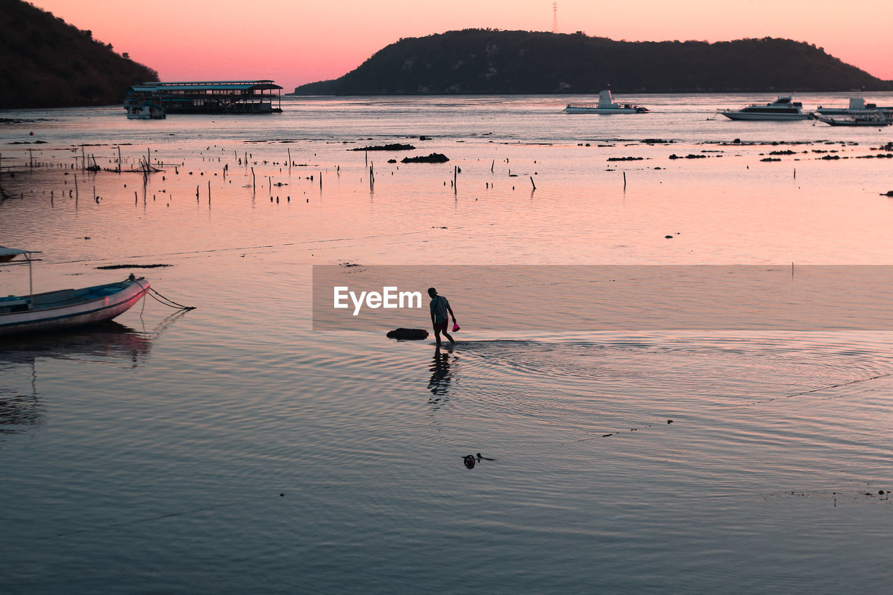 Man standing in sea against sky during sunset