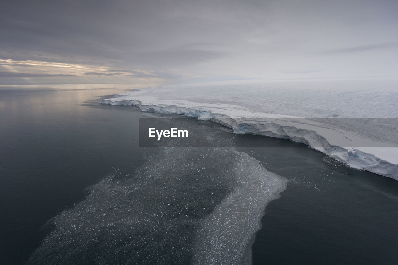 Scenic view of glacier in sea against cloudy sky during sunset