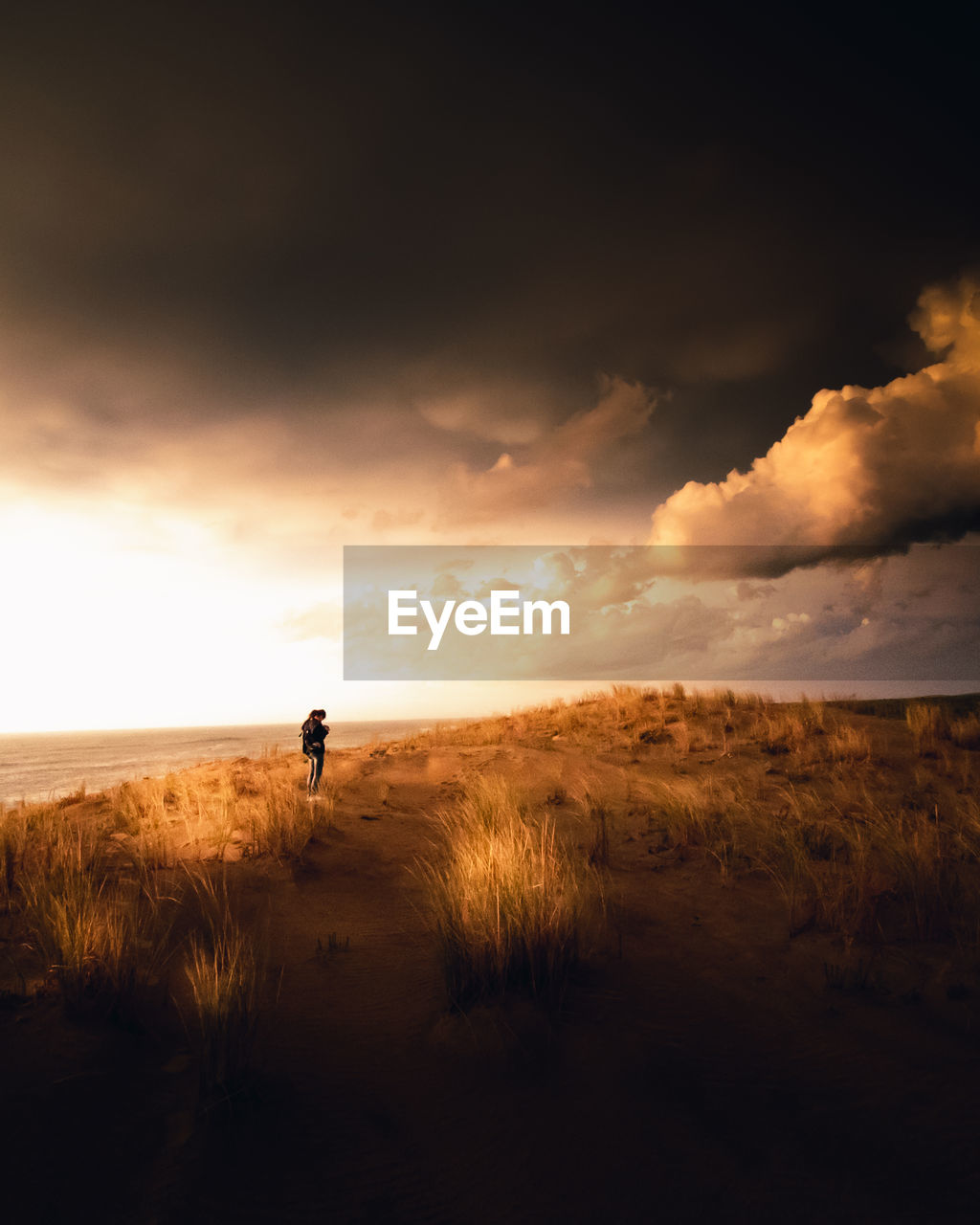 Distant view of woman standing at beach against sky during sunset