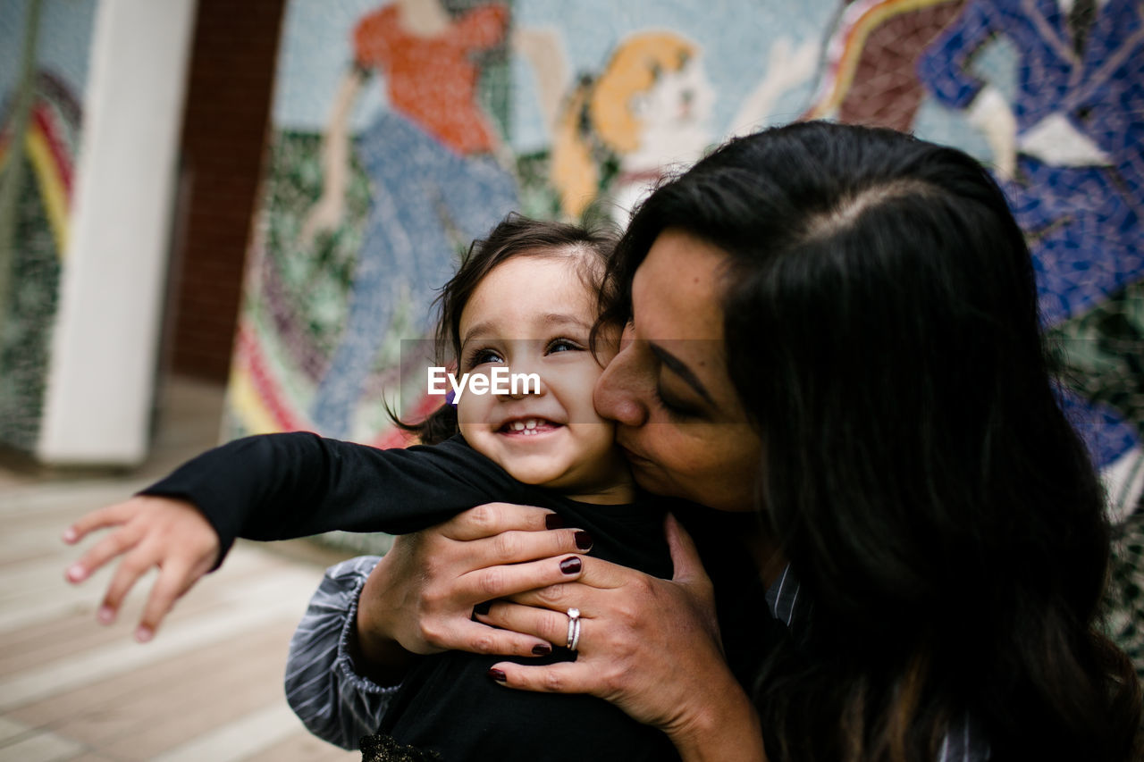 Mother kissing daughter in front of mural