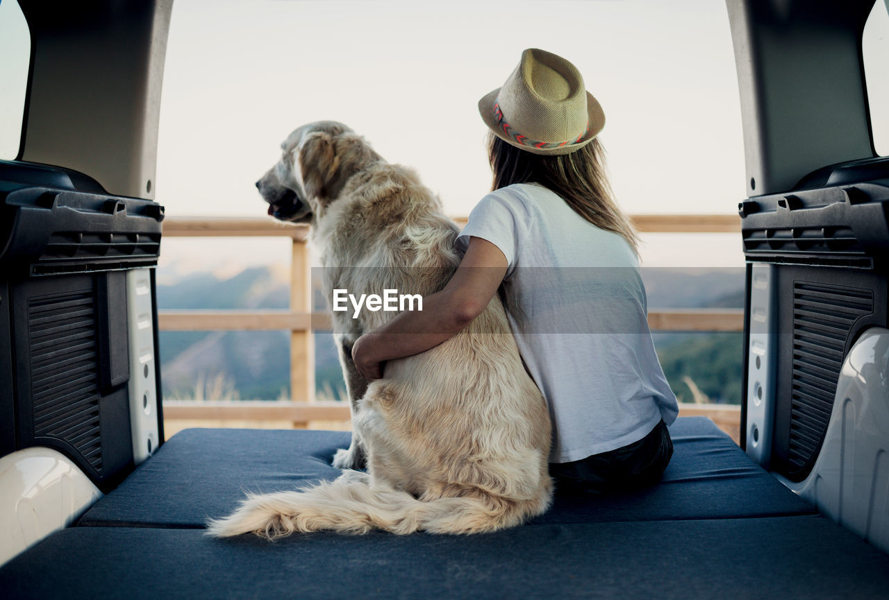 Unrecognizable female tourist embracing obedient golden retriever dog lying on mattress inside camper and admiring nature