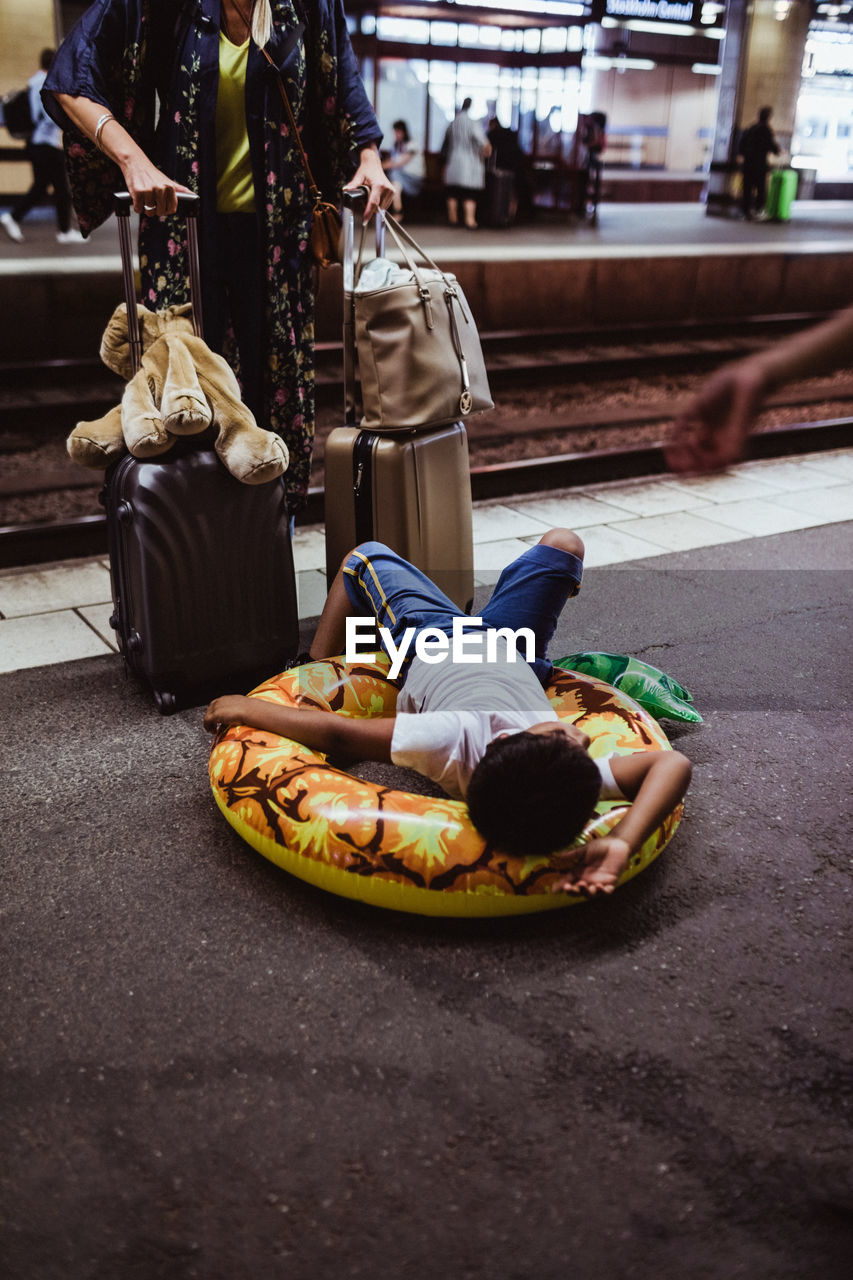 Boy lying on inflatable ring while mother standing with luggage at railroad station platform