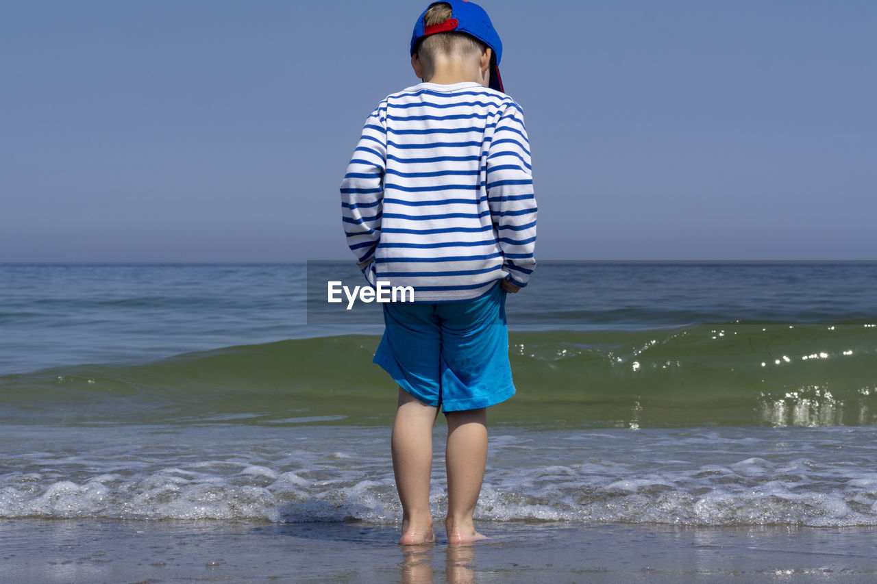 Rear view of boy standing on shore against sea at beach