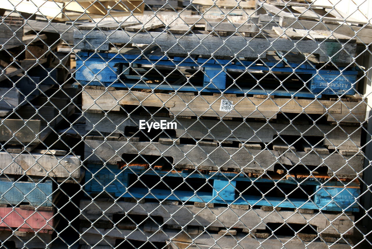 Stack of abandoned wooden crates seen through chainlink fence