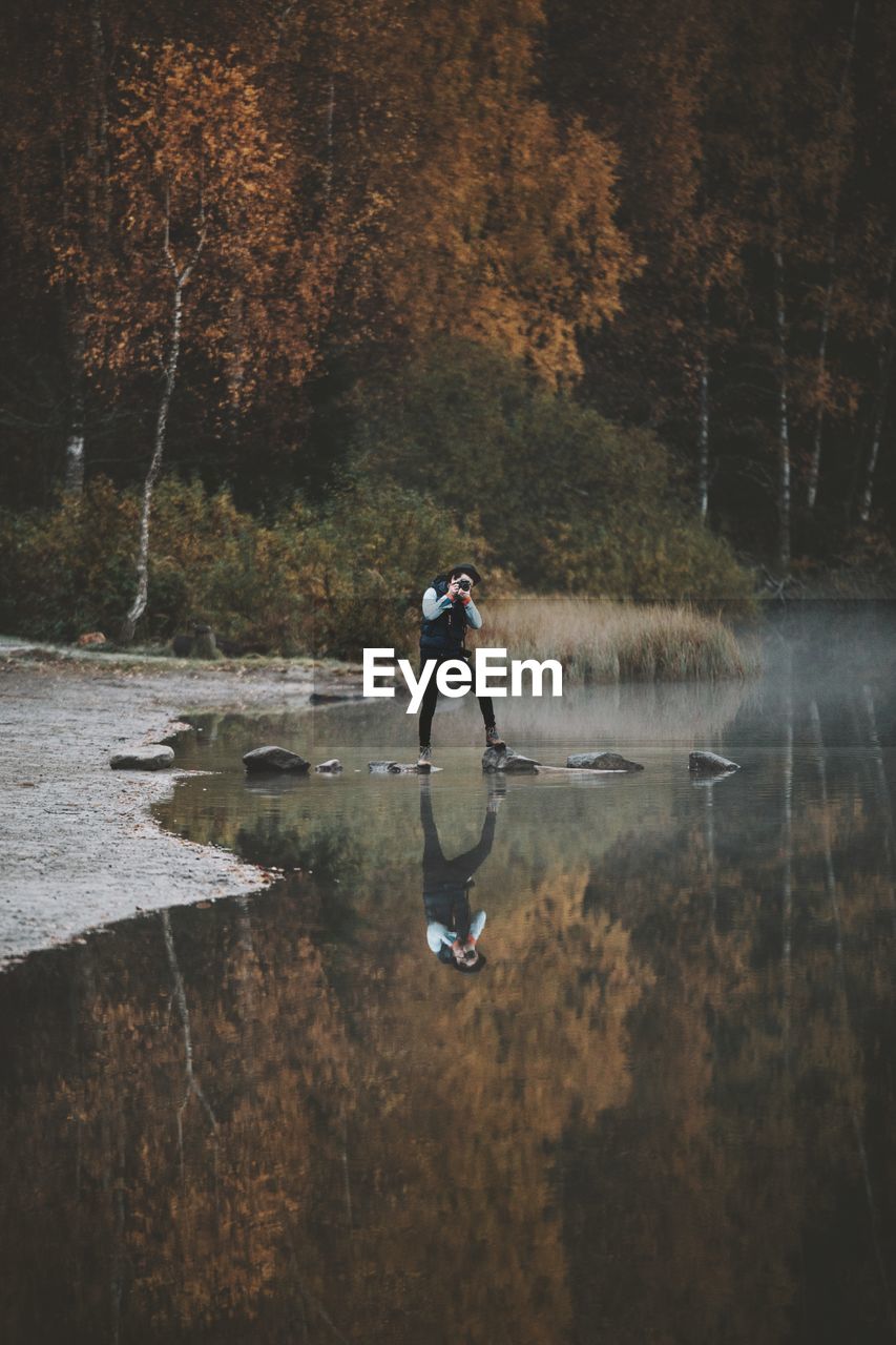 Reflection of man photographing on lake in forest