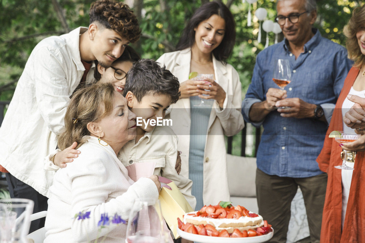 Senior woman embracing boy near family during dinner party