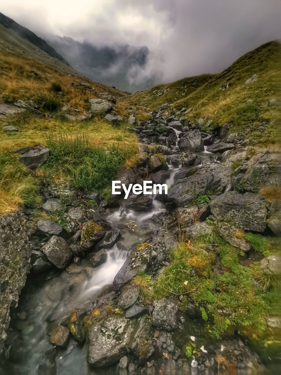 STREAM FLOWING AMIDST ROCKS AGAINST SKY