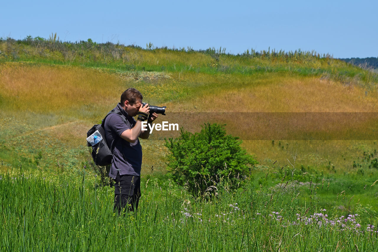 Photographer photographing on grassy field against clear sky