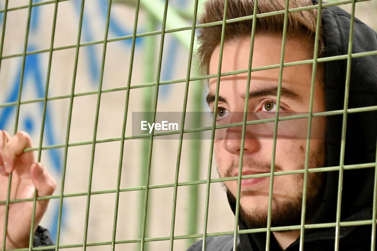 Portrait of young man looking through fence