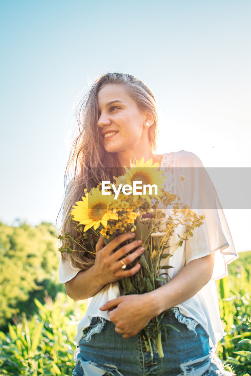 Happy woman with arms raised standing on land against clear sky