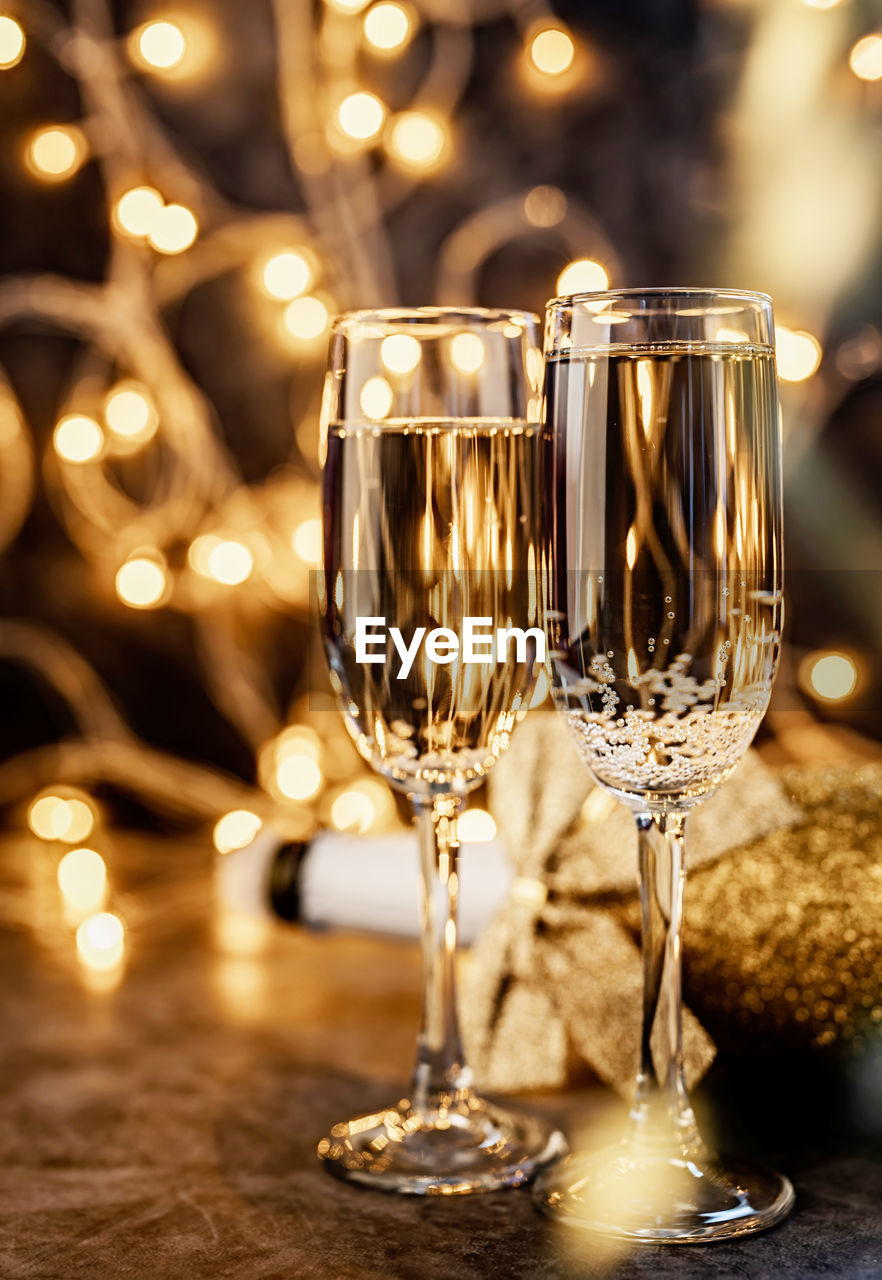 New years eve dark party table with two champagne flute, shiny bottle and christmas lights