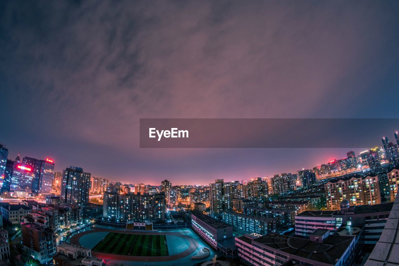 HIGH ANGLE VIEW OF ILLUMINATED CITYSCAPE AGAINST SKY AT SUNSET