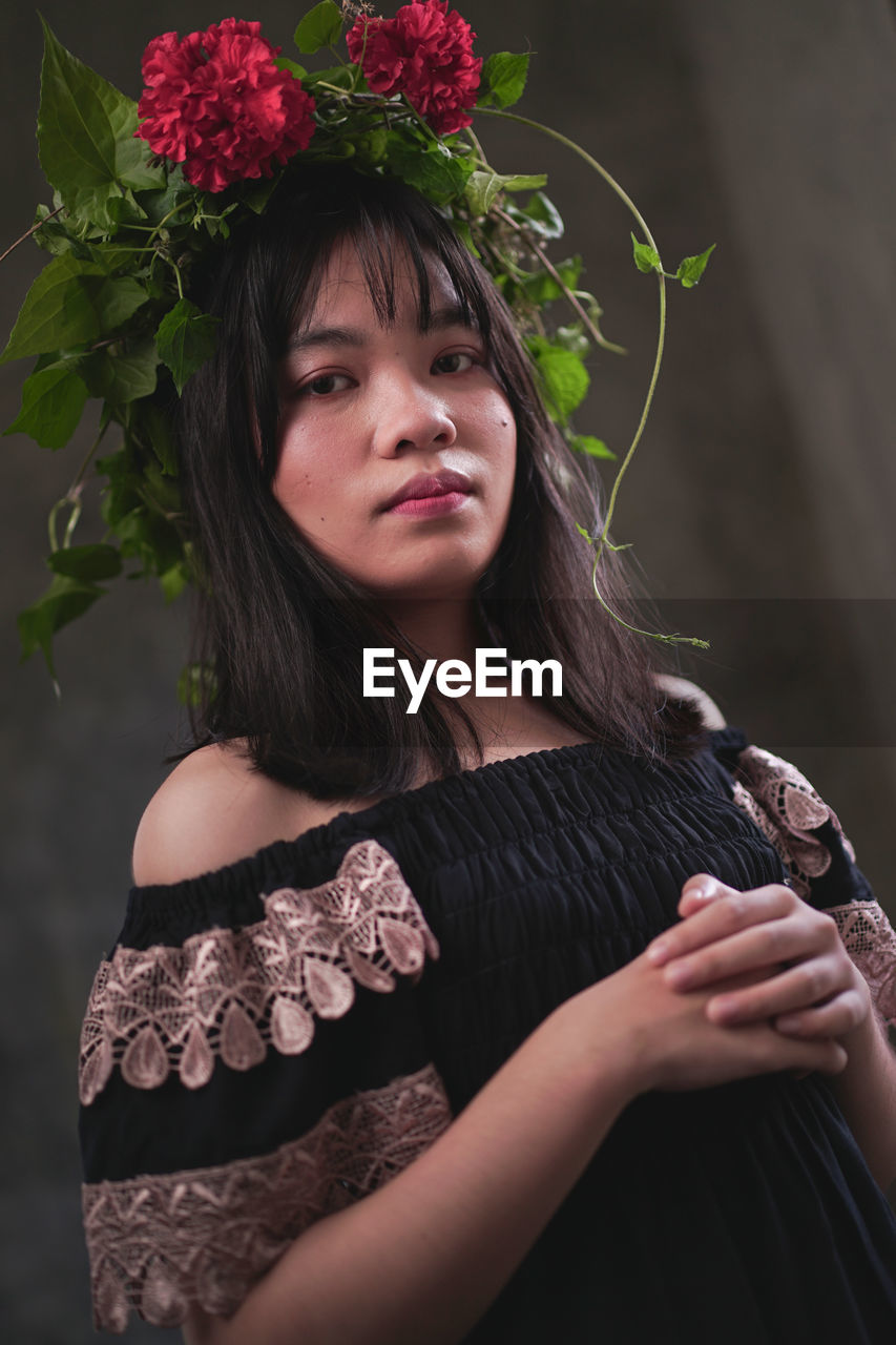 Portrait of beautiful young woman standing against red flowering plants