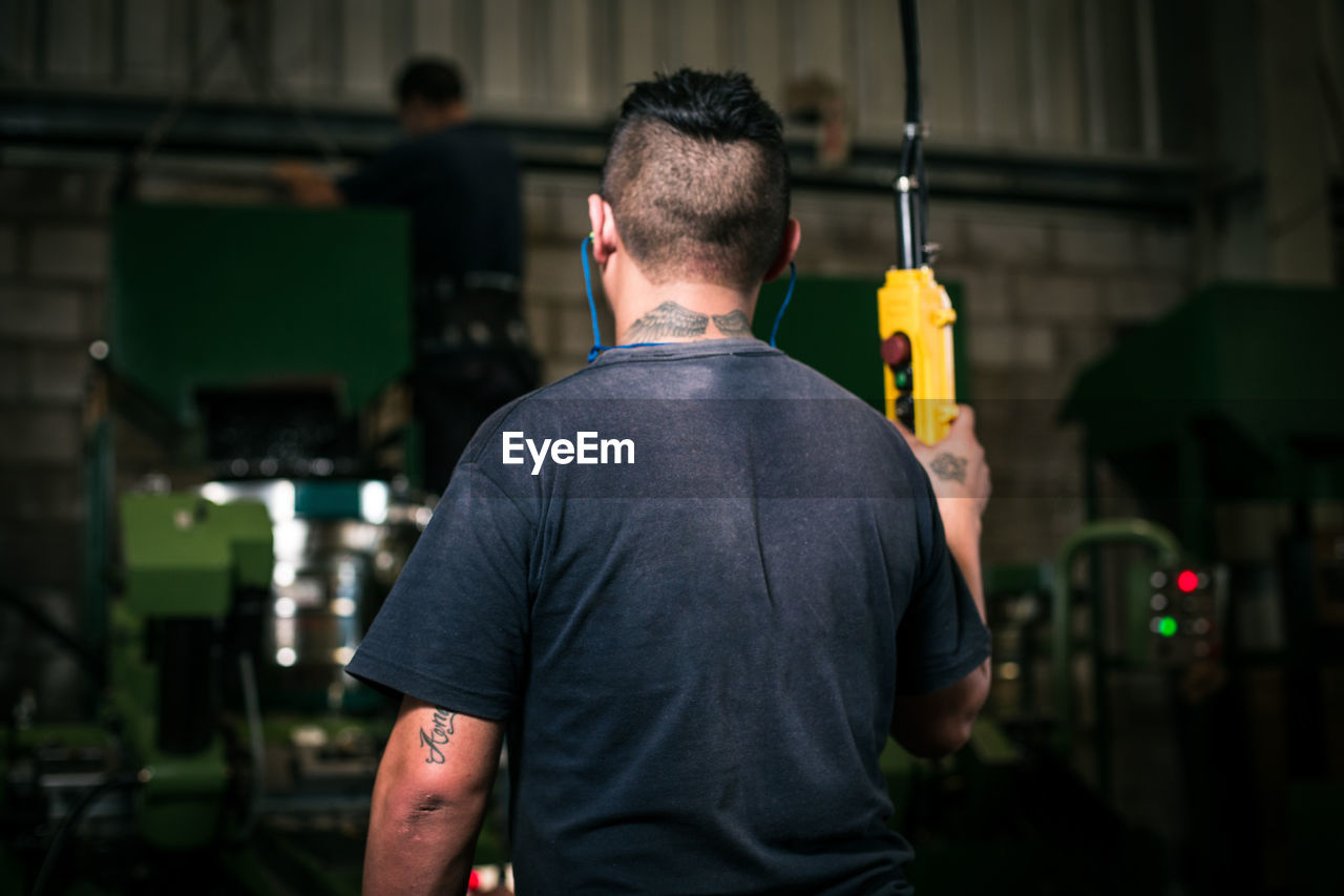 Rear view of worker operating machinery at factory