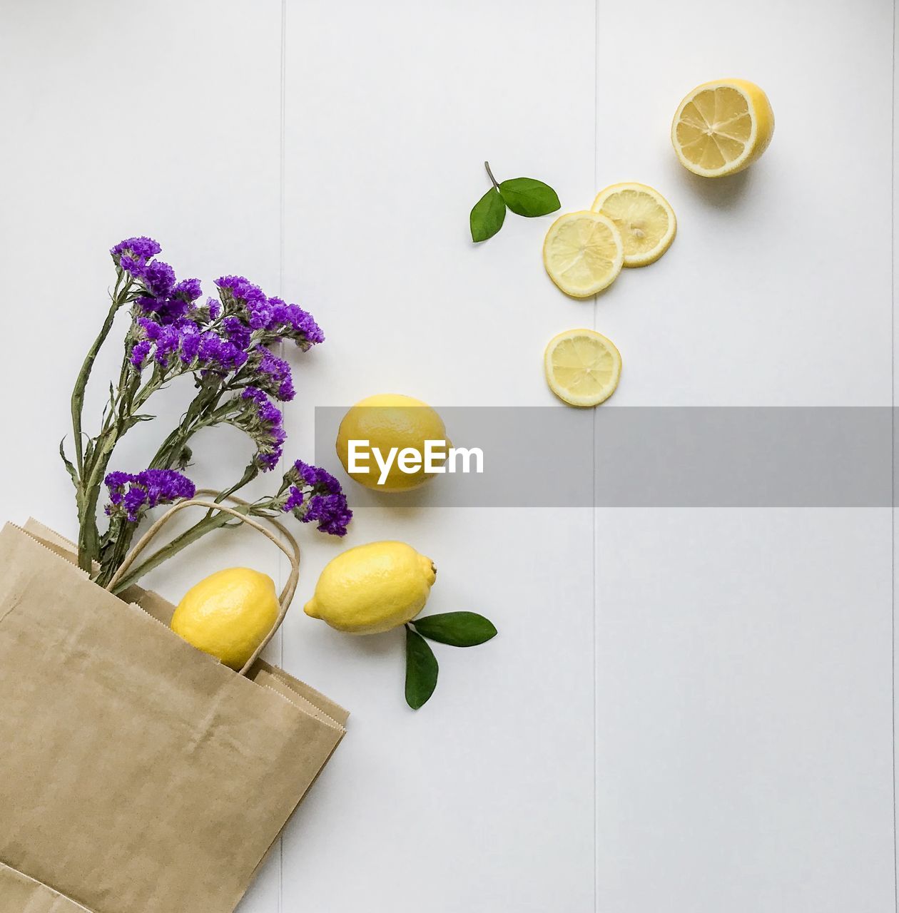 High angle view of lemons and flowers spilling from paper bag against white background