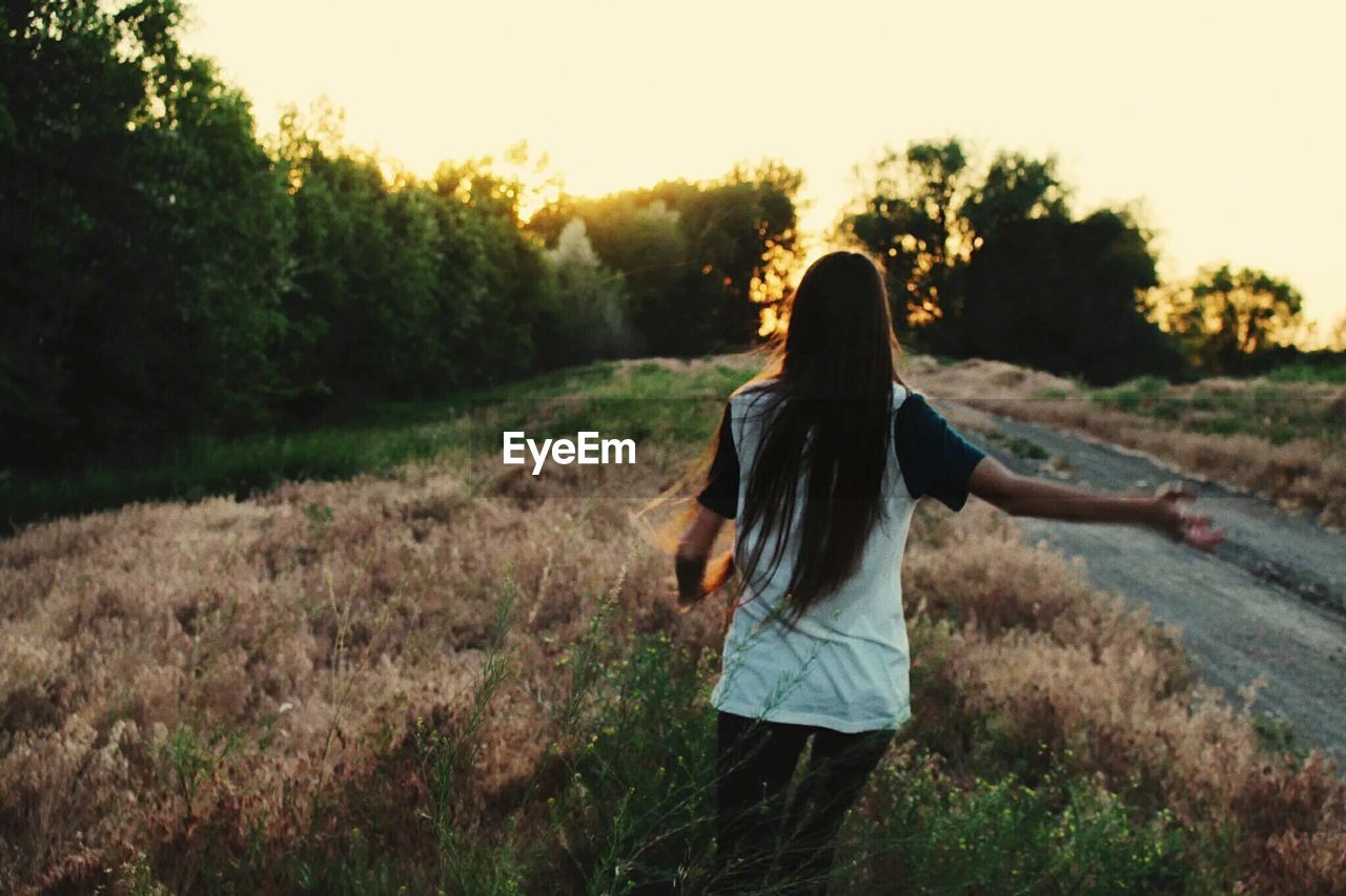 Rear view of woman standing on field during sunset