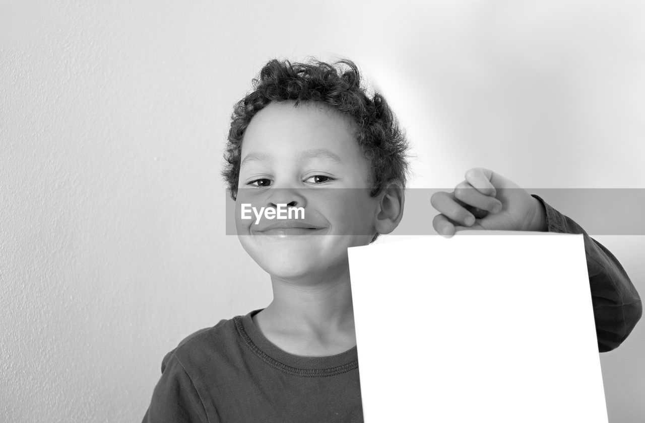Portrait of smiling boy holding paper against wall